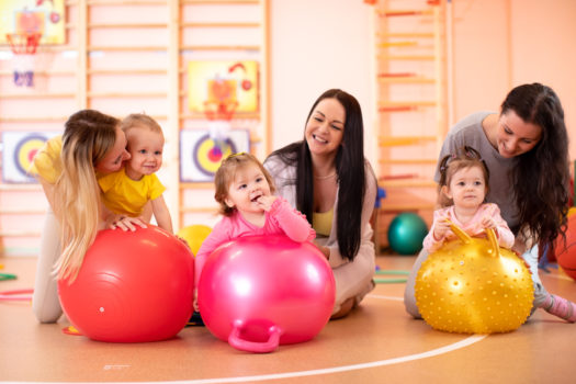 Mothers with happy babies doing exercises with gymnastic ball at fitness class. Concept of caring for the baby's health.